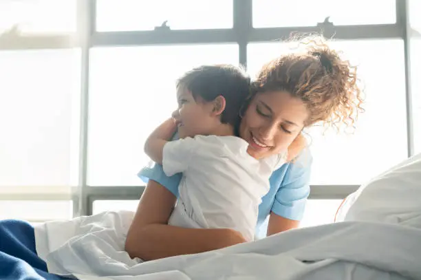 Photo of Beautiful sweet little boy hospitalized in the pediatrics ward hugging young nurse