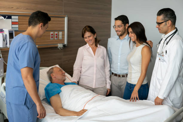 szczęśliwa rodzina odwiedzająca swojego tatę w szpitalu, podczas gdy pielęgniarka i lekarz sprawdzają starszego pacjenta - senior adult family hospital visit zdjęcia i obrazy z banku zdjęć