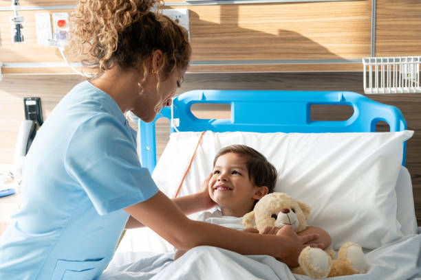 istock Friendly young nurse checking a beautiful boy lying down on hospital bed with his teddy bear smiling 1141825167
