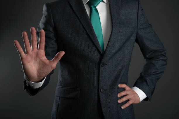Businessman. Business man is showing a stop gesture by his hand on a gray background. Shut up gesture. Stop talking concept. stop explainin stock pictures, royalty-free photos & images Businessman. Business man is showing a stop gesture by his hand on a gray background. Shut up gesture. Stop talking concept. stop explainin stock pictures, royalty-free photos & images