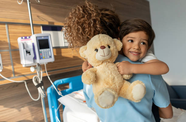 Sweet little boy looking away imagining while holding his teddy bear and hugging nurse