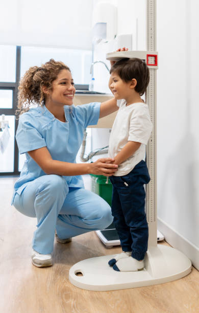 enfermera latinoamericana midiendo un paciente de pediatría comprobando el progreso del crecimiento de hos sonriendo - doctor cheerful child healthcare and medicine fotografías e imágenes de stock