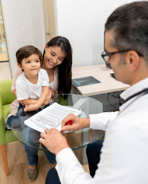 male pediatrician talking to his little patient while he looks at him and sits on mother's lap all smiling - child little boys male caucasian imagens e fotografias de stock