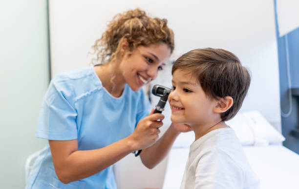Beautiful female pediatrician checking a little boy's ears both smiling