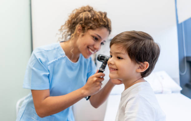 beautiful female pediatrician checking a little boy's ears both smiling - young ears imagens e fotografias de stock