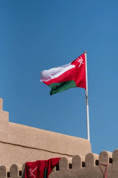 The national flag of Oman flying from a pole on the top of a small fort or defensive structure