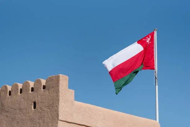 The national flag of Oman flying from a pole on the top of a small fort or defensive structure