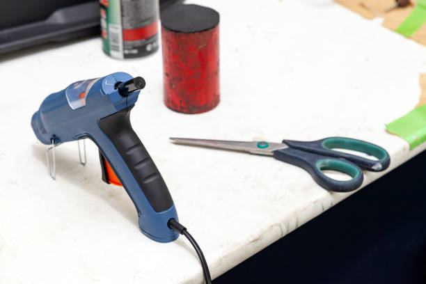 istock Electric glue gun for squeezing blue glue on the workbench for needlework in the workshop next to scissors and weighting agent for crushing surfaces 1141850911
