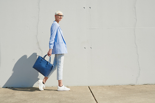 business woman outdoors with short blonde hair wearing a blue big bag, she is happy and in a positive mood