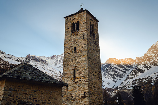 Ancient medieval bell tower of an old stone church near the mountain massif of Monte Rosa (Piedmont, Italy), in the light of the sunset