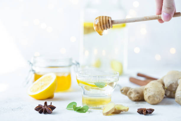 istock Honey is poured into a ginger drink in a cup. Ginger root, honey in a jar, lemon on a white table. 1141860719