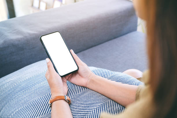 istock a woman holding black mobile phone with blank white desktop screen while sitting in living room 1141877256