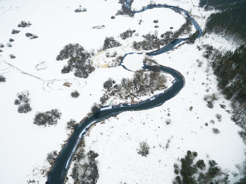 Winter landscape on the river with a forest among snow with a bird's-eye view. Drone view photo from the drone on a cloudy day. Aerial top view beautiful snowy landscape.