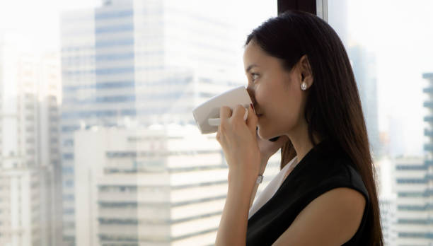 istock Businesswoman Drinking Coffee While Talking On Mobile Phone At Window 1141879941