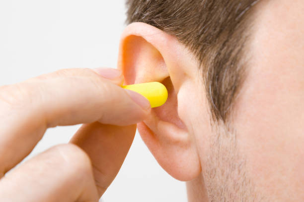 Young man's fingers putting yellow earplug into his ear on light gray background. Closeup. Young man's fingers putting yellow earplug into his ear on light gray background. Closeup. ear plug stock pictures, royalty-free photos & images