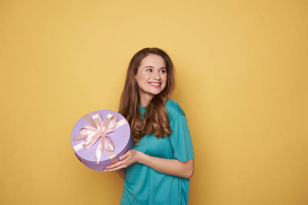 mezza lunghezza di ragazza bruna che tiene un regalo in braccio all'interno - hair bow shirt bow one young woman only foto e immagini stock