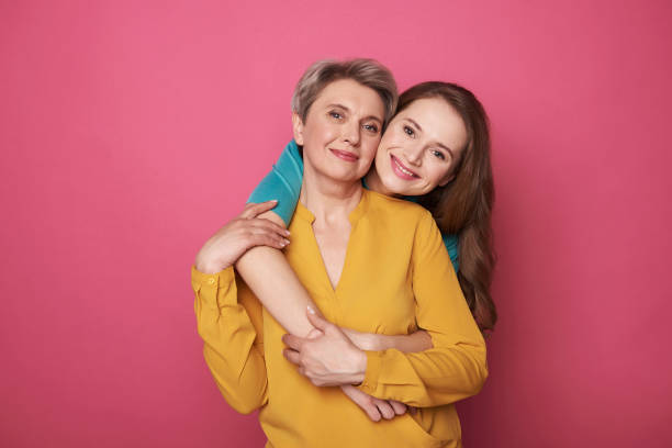 Beautiful woman with her daughter smiling and posing for camera Brunette young girl hugging her mother while standing behind and looking at camera. Trusting relationship concept daughter stock pictures, royalty-free photos & images