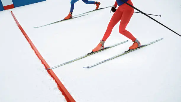 Low section of two competitors crossing finishing line during biathlon competition.