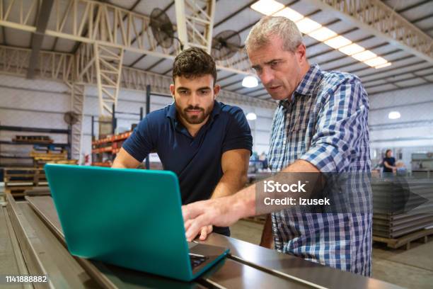 Instructor Explaining Male Trainee Over Laptop Stock Photo - Download Image Now - Instructor, Trainee, Factory