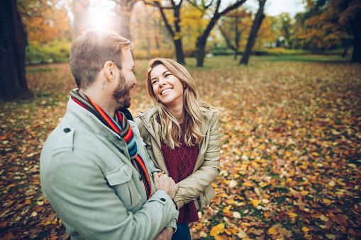 Loving couple holding hands and talking to each other in autumn day at the park.