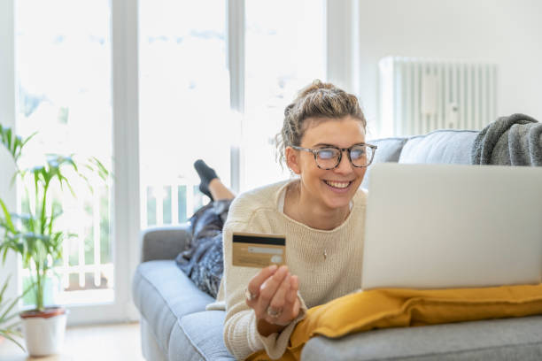 женщина покупки онлайн с кредитной картой у себя дома на диване - lying down women laptop freedom стоковые фото и изображения