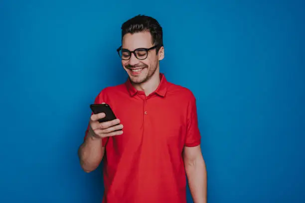 Photo of Waist up of happy Caucasian man holding smartphone in arm indoors