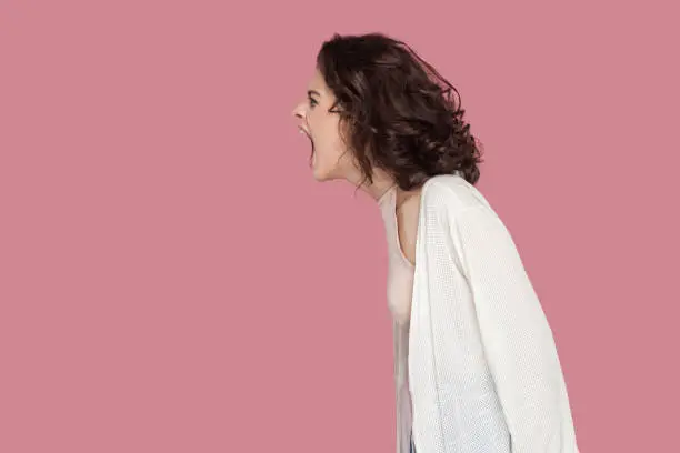 Photo of Profile side view portrait of brunette young woman with curly hairstyle in casual style standing and screaming. people expression and emotion.