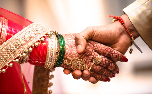 coppia indiana indù che si tiene per mano durante il loro matrimonio simboleggiando l'amore e l'affetto. le mani della sposa sono decorate magnificamente dall'arte mehndi indiana insieme a gioielli e braccialetti colorati - fidanzamento foto e immagini stock