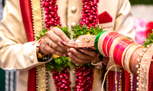 Engagement Ring ceremony- Indian Hindu male putting ring on bride's decorated finger. Couple is well attired as per traditional Indian Hindu wedding. Groom wearing Jodhpuri suit and floral garland. Beautiful photo of a ring ceremony being held as per Hindu rituals. Bridegroom is putting a ring to her Bride. Both dressed in traditional hindu marriage attire. hinduism stock pictures, royalty-free photos & images