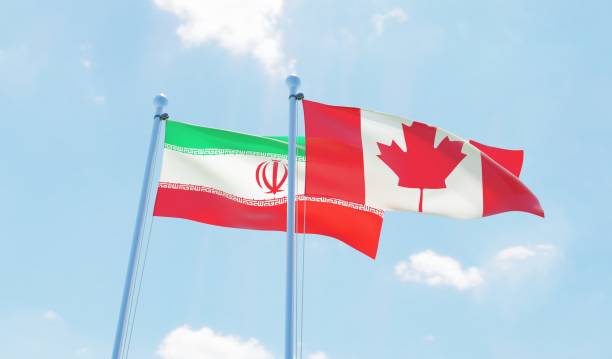 istock Canada and Iran, two flags waving against blue sky 1141910732