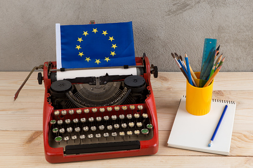 Political, news and education concept - red typewriter, flag of European Union, notebook and stationery on gray cement background