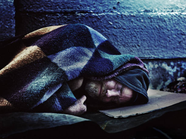 Homeless man sleeping on sidewalk A homeless man sleeps under a ratty blanket on a hard stone sidewalk homeless person stock pictures, royalty-free photos & images