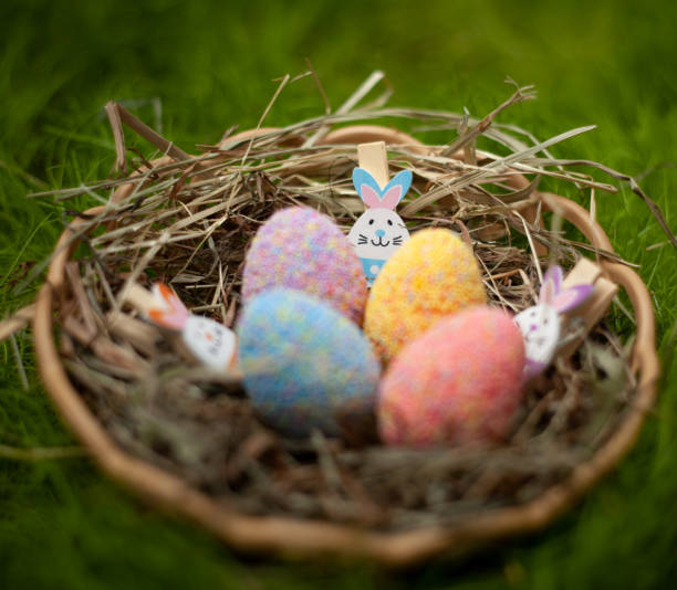 istock Decorative Easter colored eggs in a basket with hay decorated with Easter rabbit figurines on a green lawn 1141928377