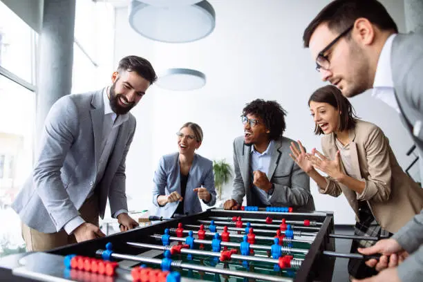 Happy young office workers playing table football