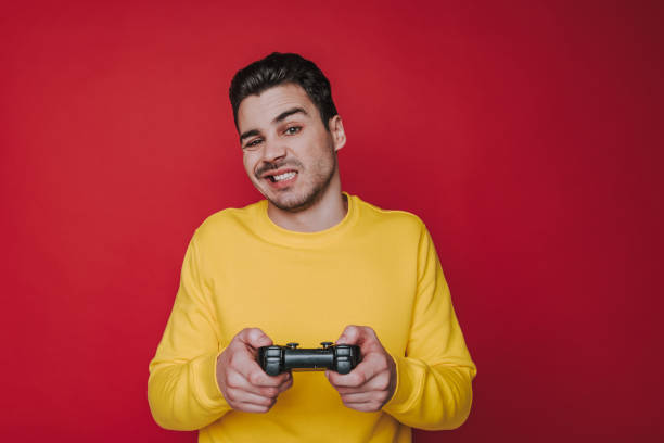 istock Half length of unpleasant guy squinting and holding joystick on red background 1141939151
