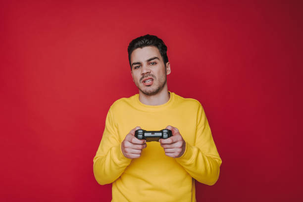 istock Half length of unpleasant brown-haired guy holding joystick on red background 1141939155