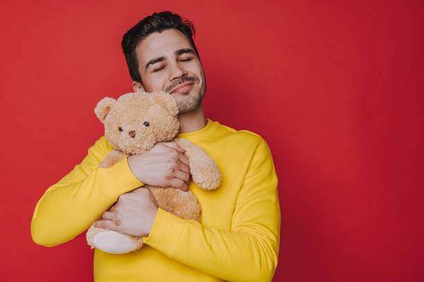 Waist up of happy unshaven man hugging teddy bear on red background stock photo