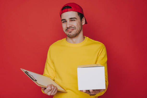 istock Young guy in cap holding a box and clipboard in arms 1141939197