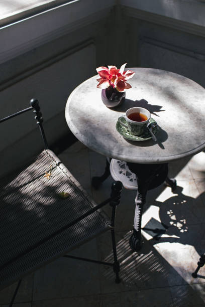 Beautiful vintage porcelain cup with black tea on table with orchid and sunlight shadows. Afternoon tea ceremony.