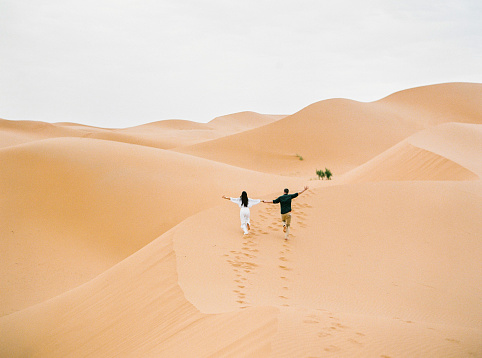 Young couple enjoying the sunset in dunes. Romantic traveler walking on the Sahara desert. Adventure travel lifestyle concept.
