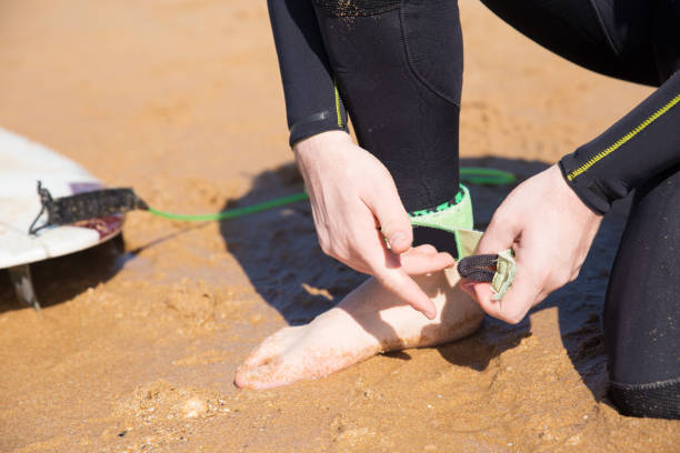 istock Closeup of young man putting on surfboard leash on beach 1141945396