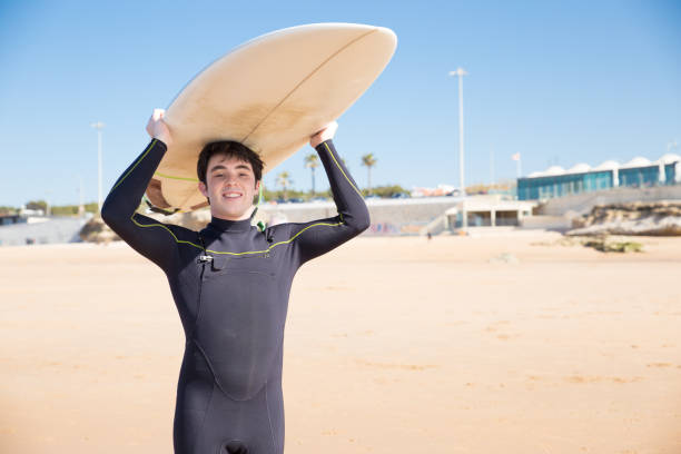 istock Happy young man holding surfboard on head on sunny beach 1141945414