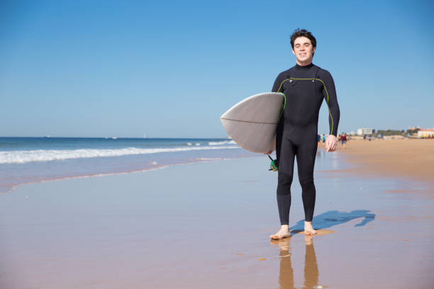 istock Happy young man holding surfboard on summer beach 1141945417