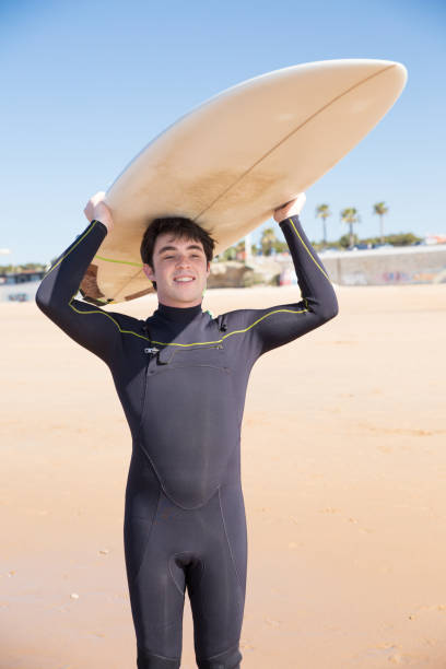 istock Smiling man holding surfboard on head on sunny beach 1141945429