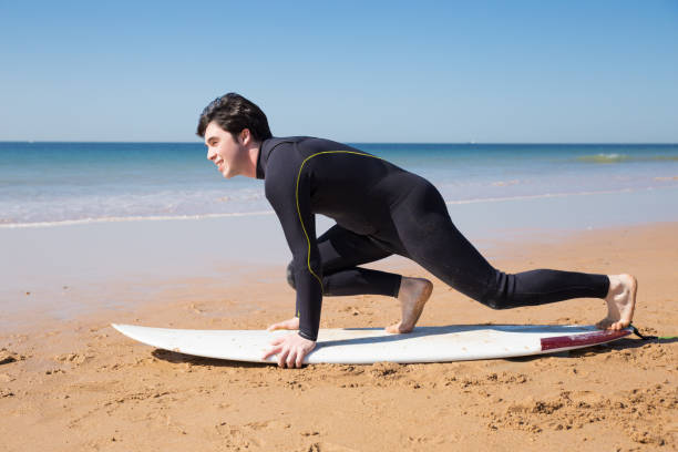 istock Smiling attractive man learning to stand up on surfboard on beach 1141945432