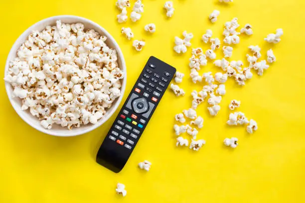 Photo of Popcorn and remote control viewed from above on yellow background. Flat lay of pop corn bowl. Top view