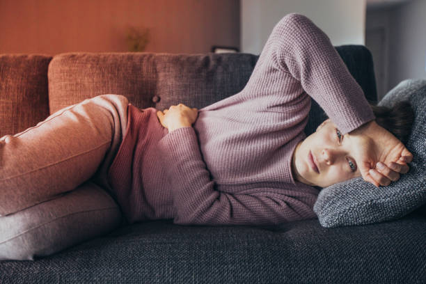 istock Sick woman lying on sofa, holding hands on stomach and head 1141946777