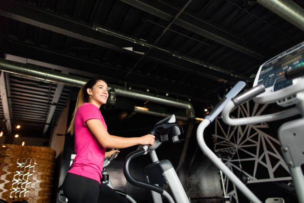 istock Smiling young woman on an elliptical machine 1141947731