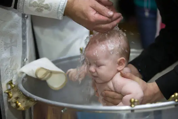 Priest pours water on the infant at baptism. Orthodox rite of baptism. Acceptance of faith. Child in the font