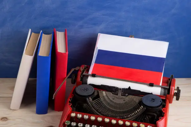 Political, news and education concept - red typewriter, flag of the Russia, books on table against the background of the blue school board